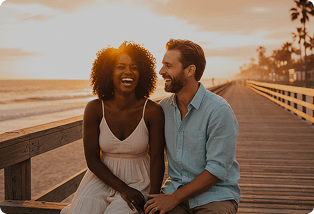 Couple laughing together on a boardwalk at sunset